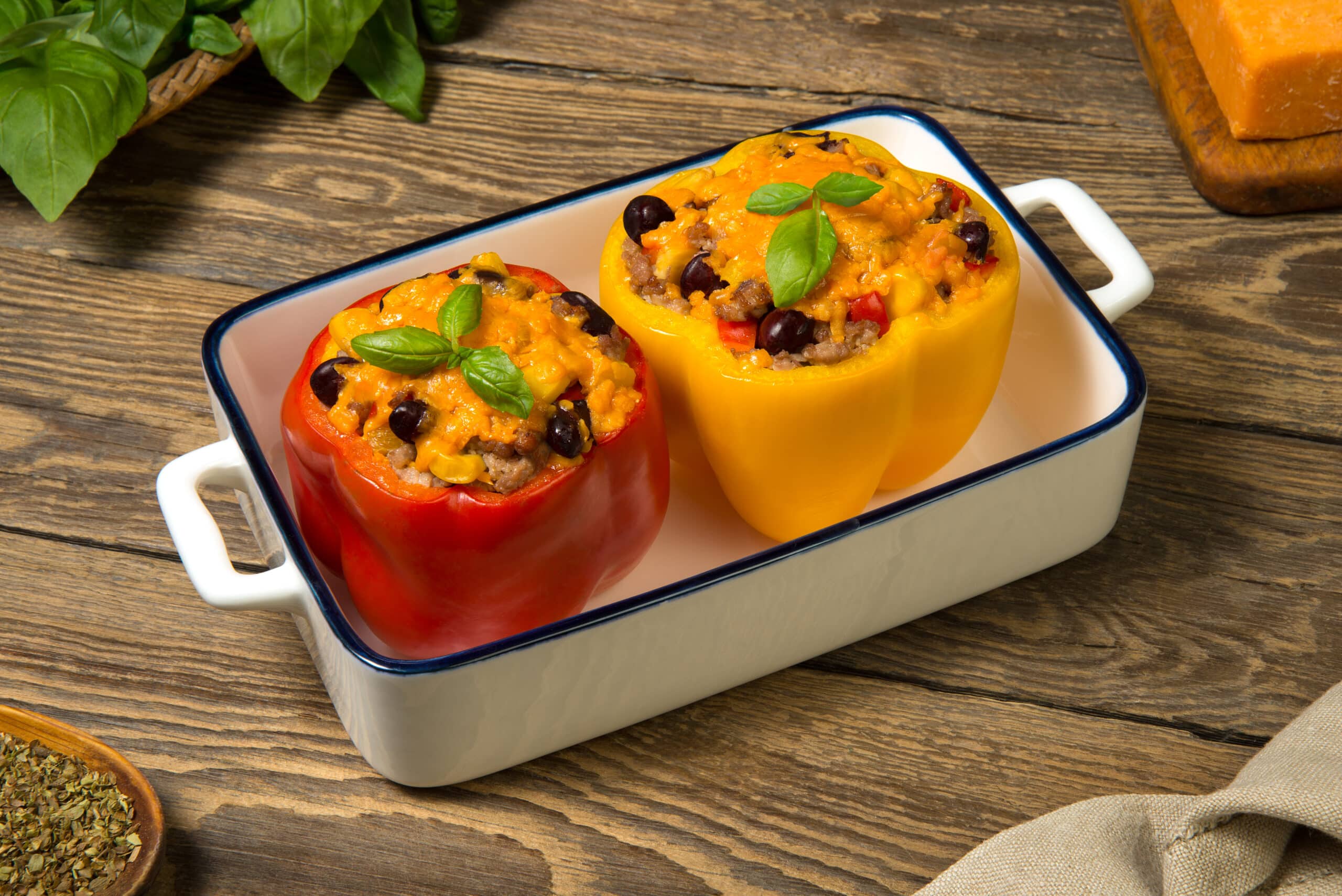 Bell Peppers Stuffed With Meat And Vegetables, Baked With Cheese In A White Casserole On An Old Rustic Table. Close Up.