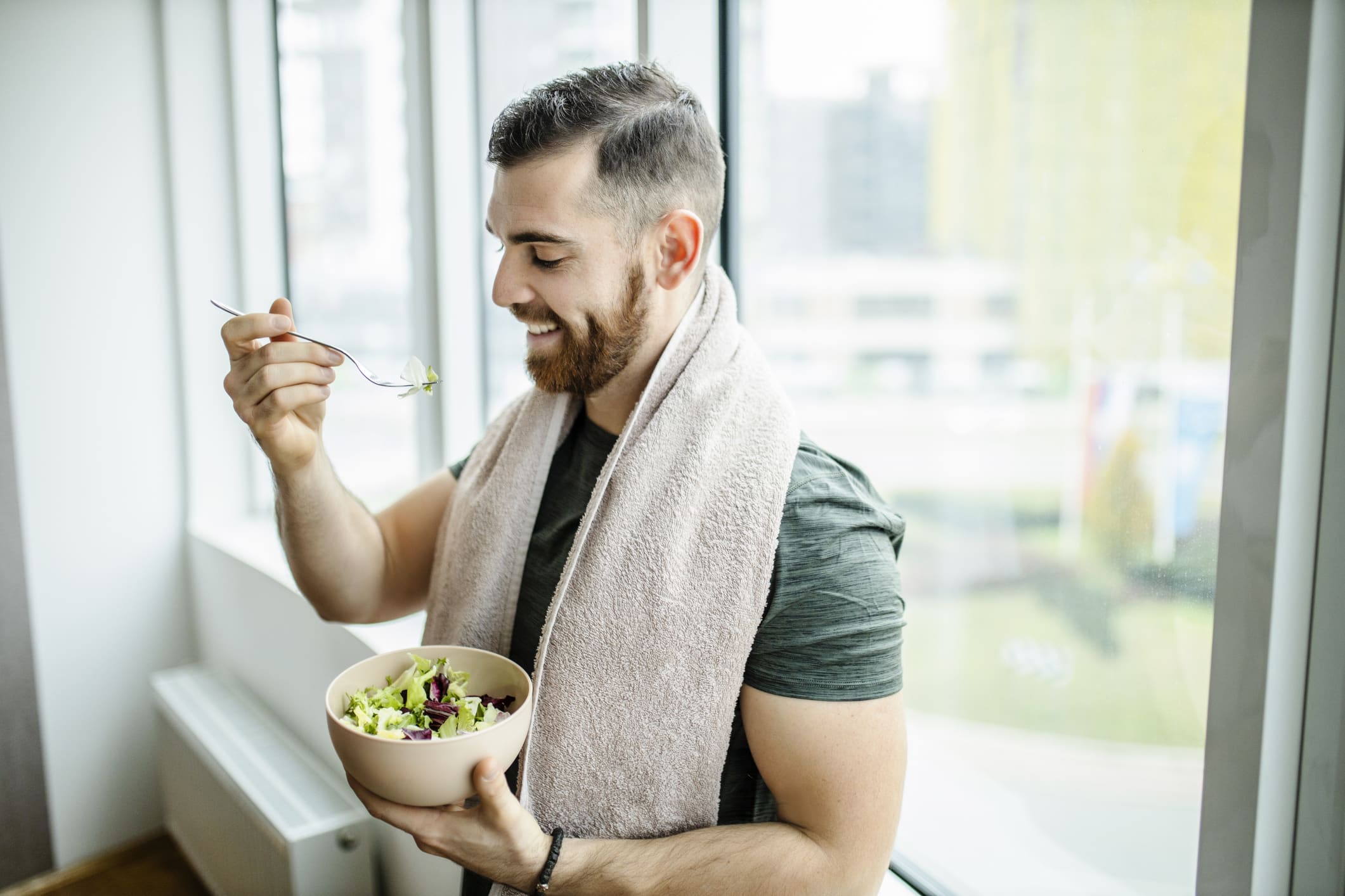 Young Man Eating Fresh Salad After Intensive Home Workout