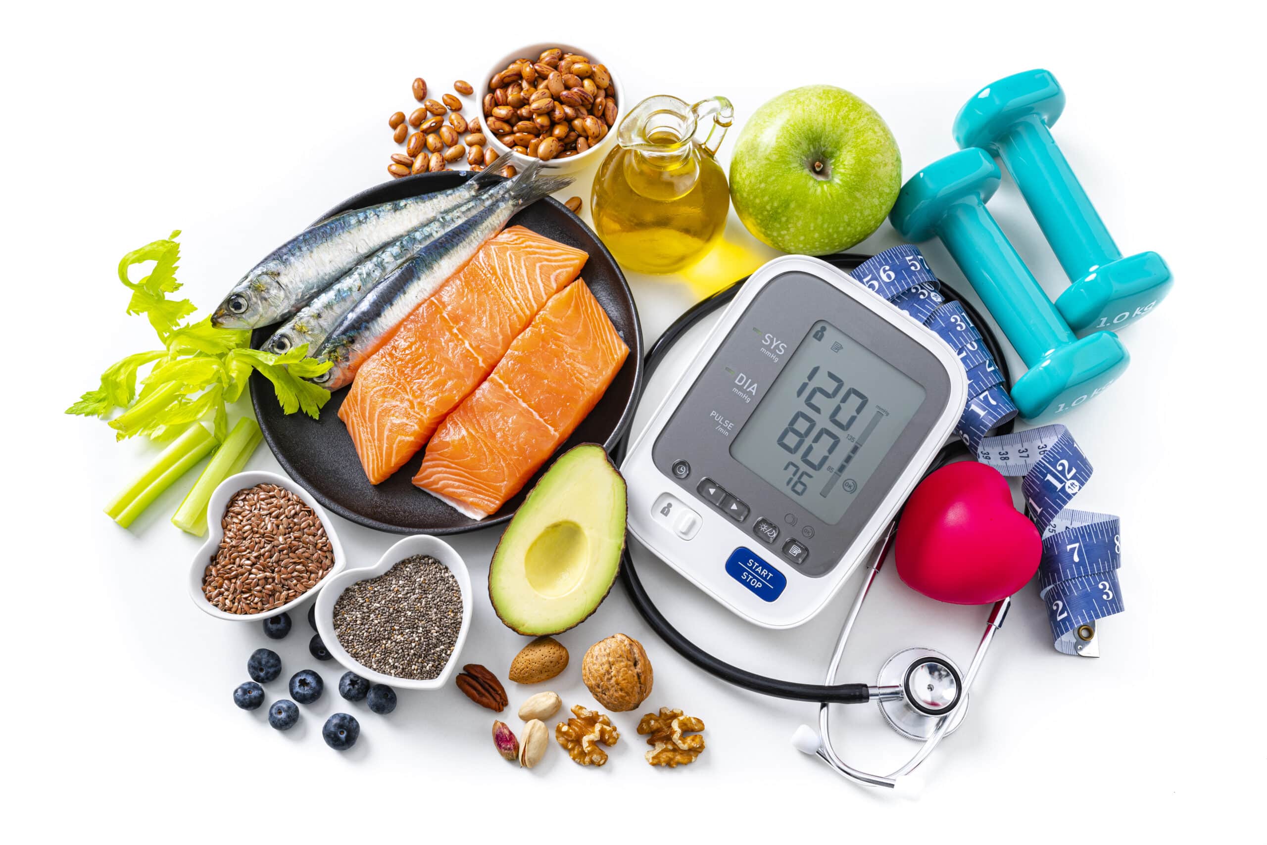 Overhead View Of A White Background Filled With Multicolored Healthy Food. A Blood Pressure Monitor, Stethoscope And Dumbbells Complete The Composition. The Composition Includes Salmon, Sardines, Green Apple, Nuts, Blueberries, Olive Oil, Dates, Celery, Avocado, Broccoli, Pinto Beans, Chocolate, Flax Seeds Among Others. High Resolution 42Mp Studio Digital Capture Taken With Sony A7Rii And Zeiss Batis 40Mm F2.0 Cf Lens