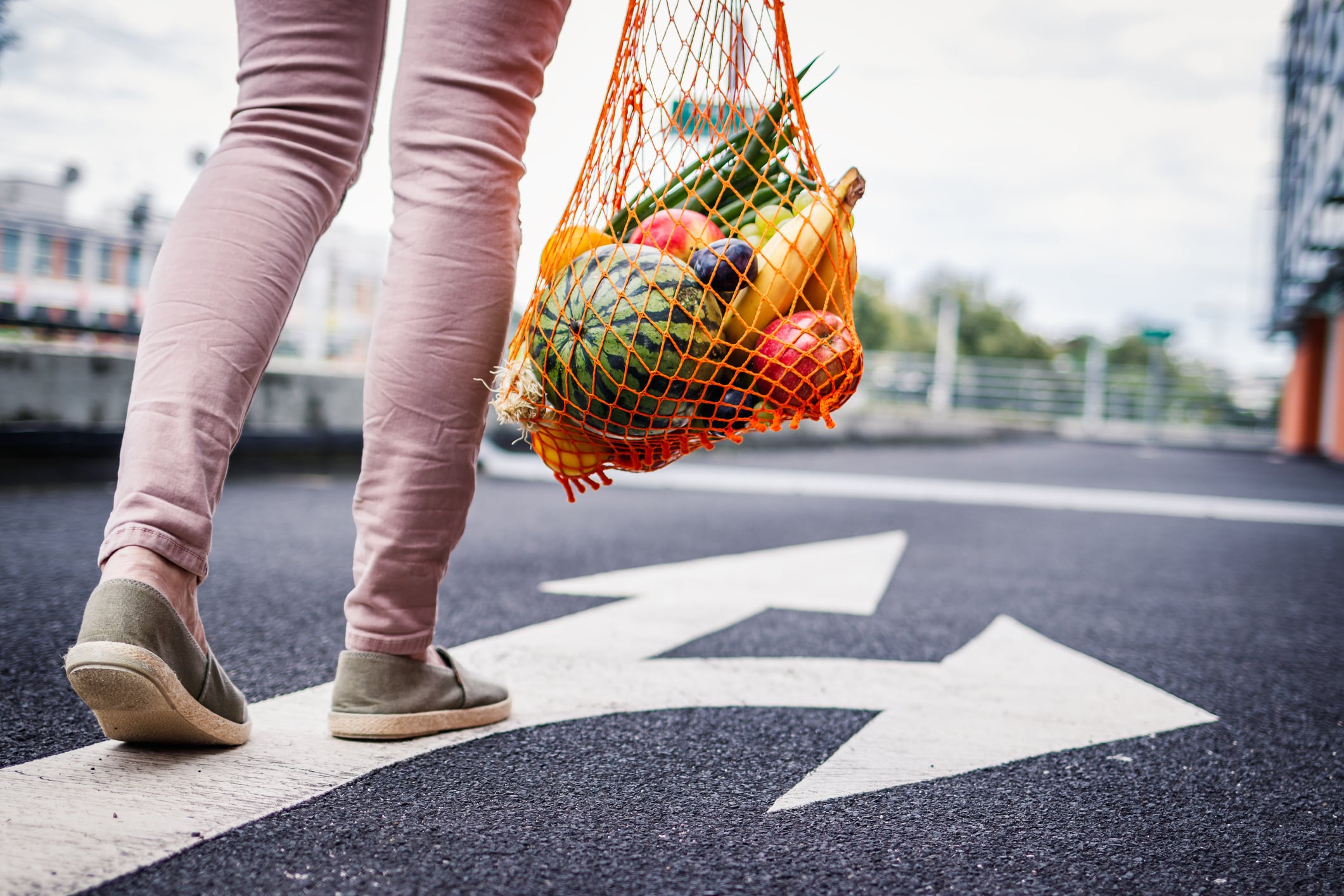 Plastic Free Shopping. Woman With Reusable Mesh Bag Full Of Fruit Walking On The Road From Supermarket