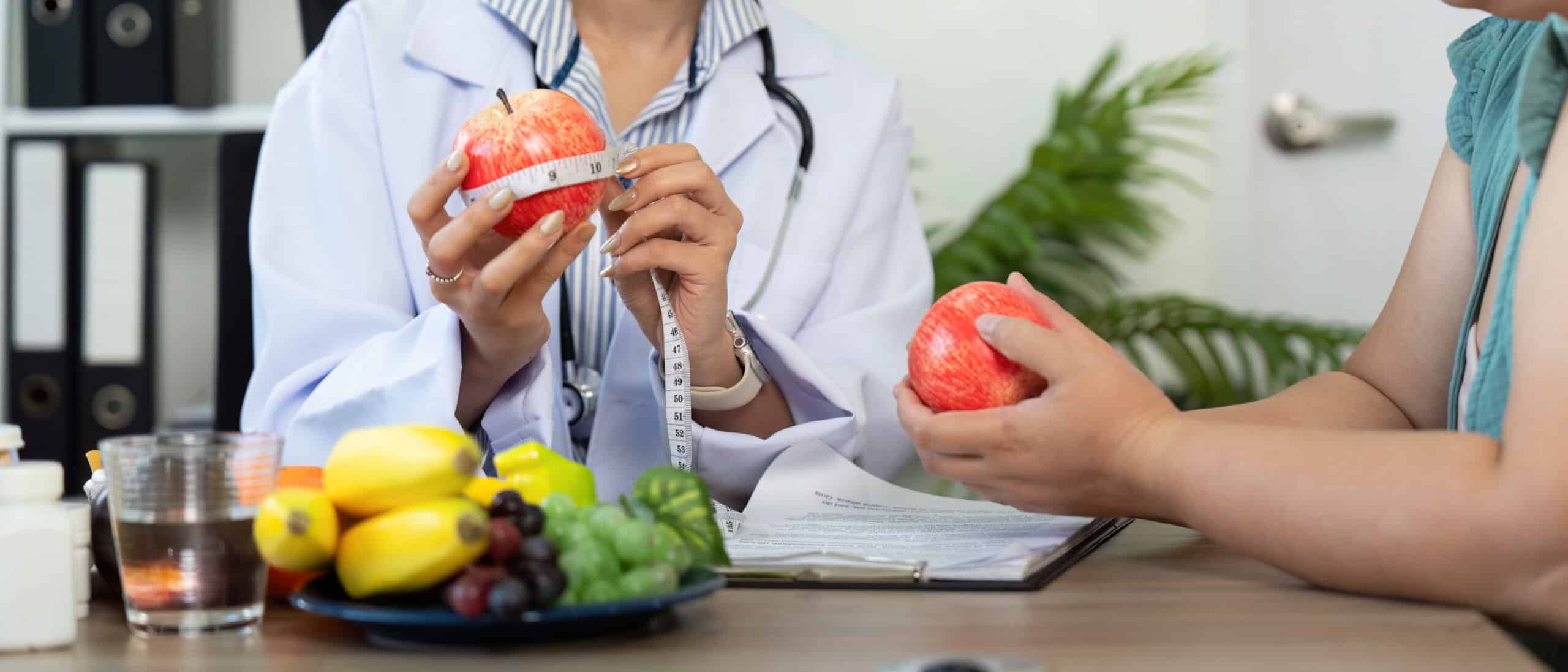 During The Consultation, The Nutritionist Measures The Apple To Discuss Portions, Illustrating A Comprehensive Approach To Nutrition In A Supportive Setting.