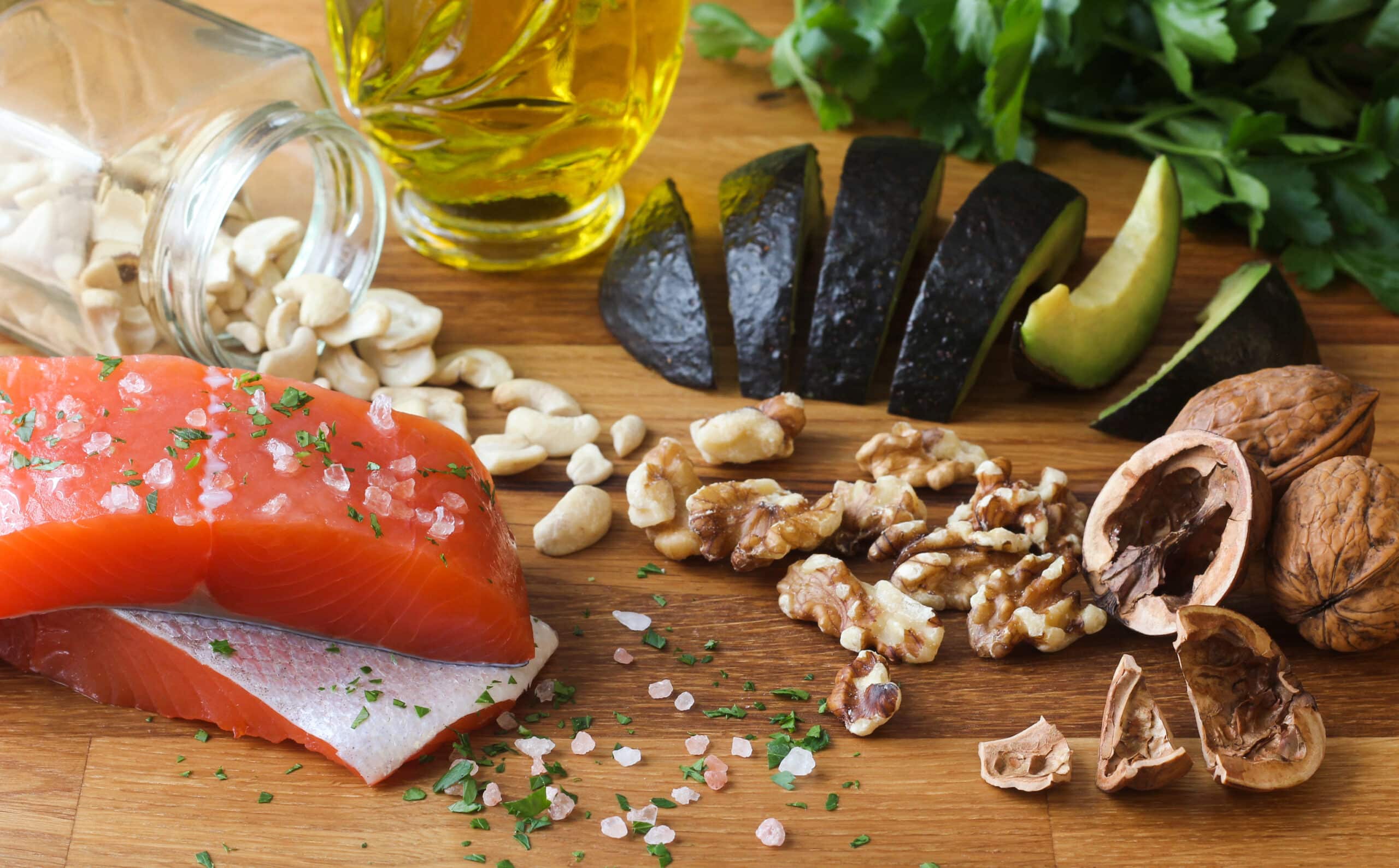 Salmon Seasoned With Salt, Cashews, Walnuts, Sliced Avocado, And Olive Oil On A Butcher Block, Garnished With Parsley.