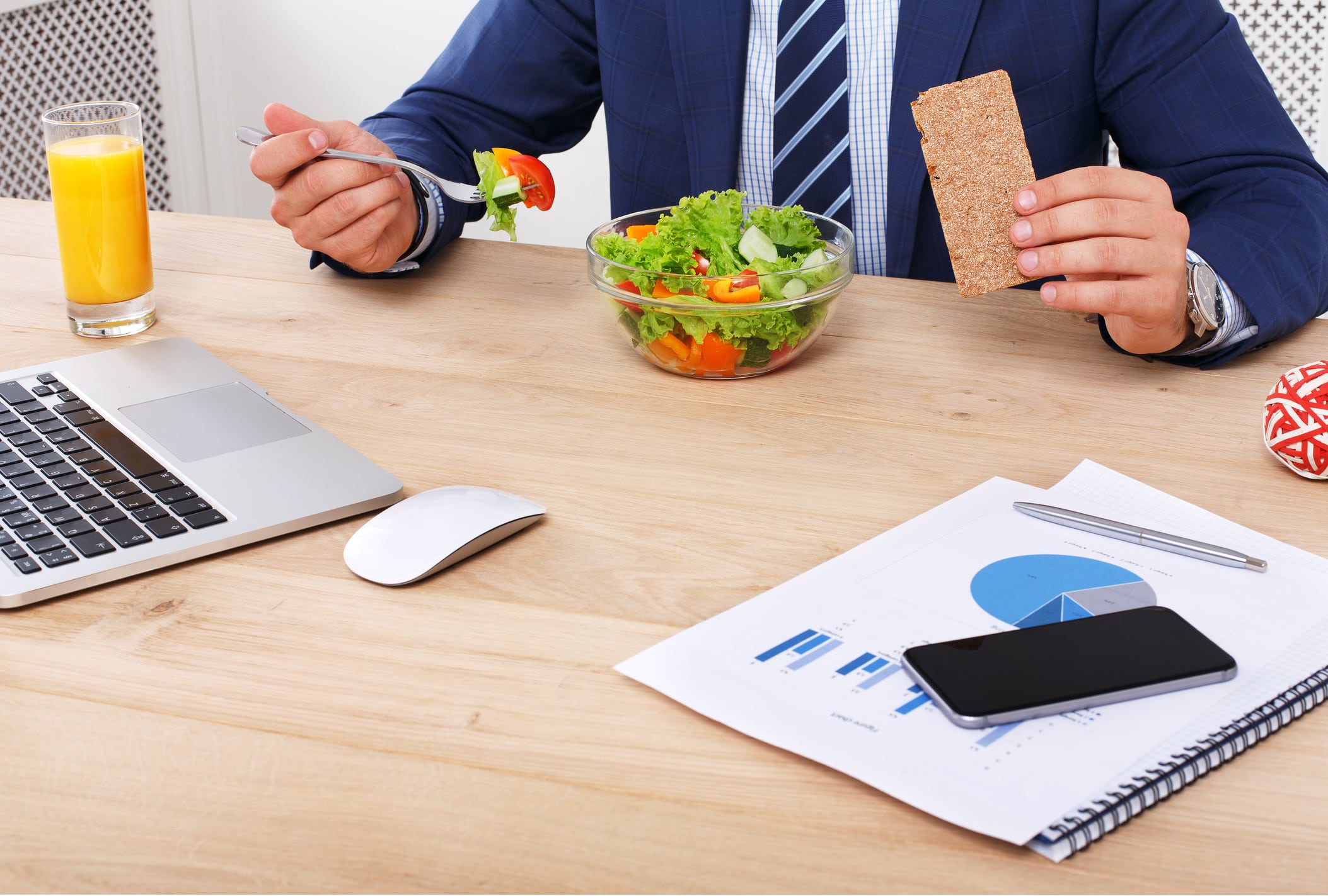 Business Lunch At Working Place. Businessman In Office. Healthy, Diet Food, Vegetable Salad With Orange Juice. Cell Phone, Laptop And Papers, Fitness Bracelet On Hand.