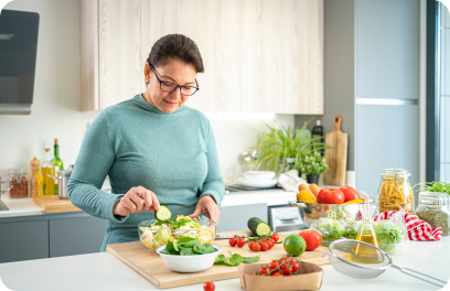Building a salad, a person stands in their kitchen surrounded by different vegetables and kitchen utensils.