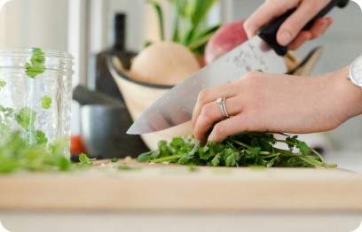 Persons hands are seen as they chop up cilantro.