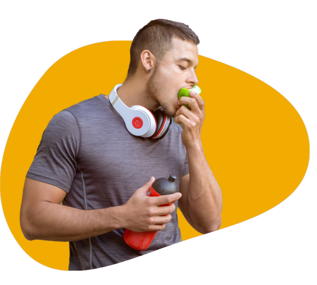 A young man in workout outfit with headphones around his neck and eating an apple