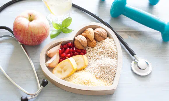 Heart shape plate containing different healthy food and a stethoscope present on a table