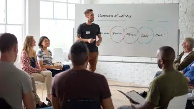 A group of people sitting in a circle and one man giving a presentation on whiteboard