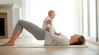 A mother in glute bridge position with a baby on the belly and playing with it