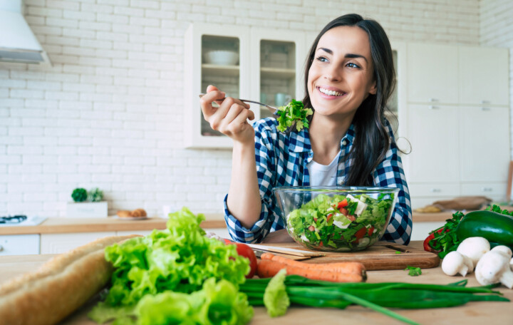 Person sitting with vegetables around them as they eat a salad