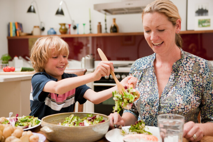 Son helping to serve salad for mother at the family dinner table