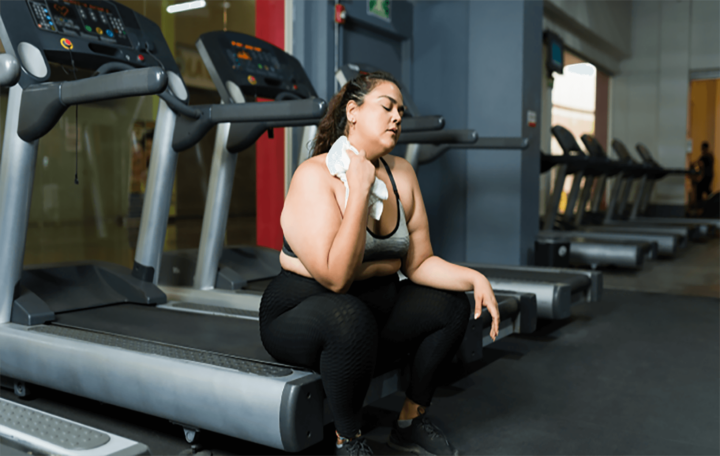 Person sits on a treadmill after working out, patting away sweat with a towel.