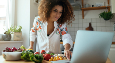 Person leans over their kitchen counter as they look up recipes from their dietitian on their laptop.