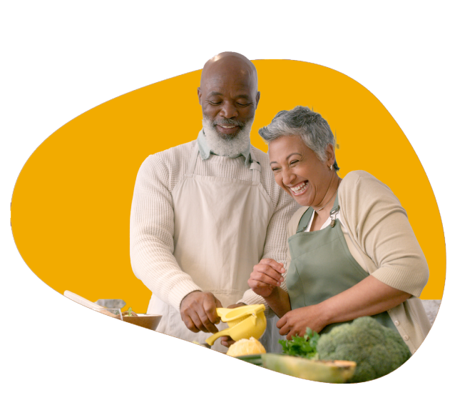 A couple stand next to each other cooking a meal that is high cholesterol approved.