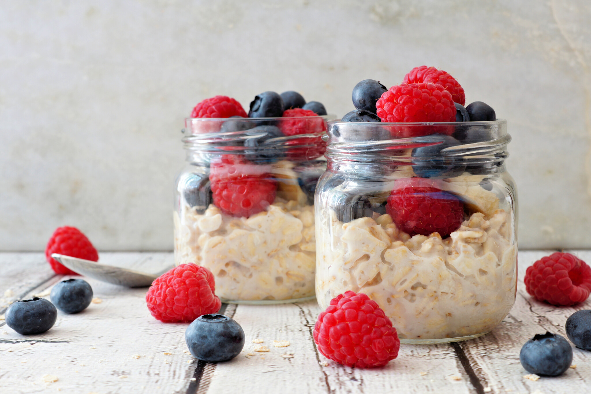 Overnight oats with fresh blueberries and raspberries in jars with a white background