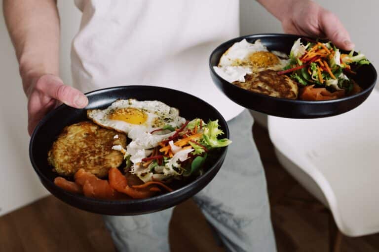 Two Balanced Breakfast Bowls With Eggs, Vegetables, And Smoked Salmon Being Served.