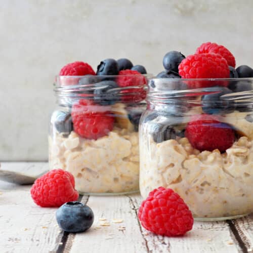 Overnight Oats With Fresh Blueberries And Raspberries In Jars On A Rustic White Wood Background