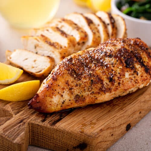 Grilled Chicken Breast Whole And Sliced On A Cutting Board With Fresh Lemon