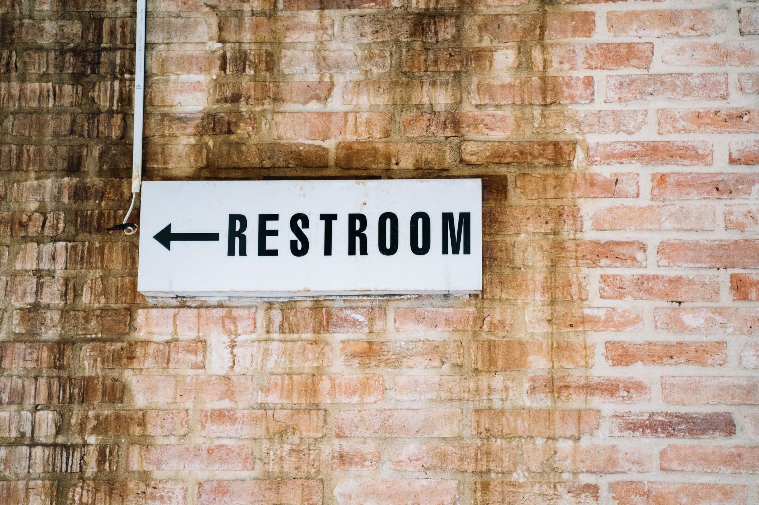 Restroom Sign With An Arrow On A Brick Wall, Representing Gi Side Effects Of Glp-1 Medications Like Diarrhea And Constipation